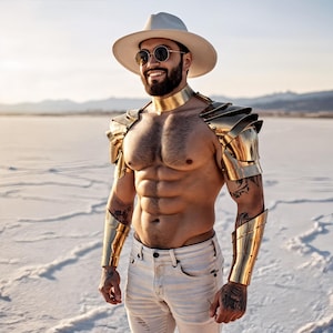 May include: A person wearing a cream-colored hat, round sunglasses, and gold-colored armor. The armor includes a neck piece, shoulder pads, and arm cuffs. The person is also wearing light-colored jeans.
