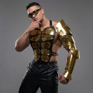 Könnte beinhalten: Ein Brust- und Armpanzer-Set aus schwarzem Leder und goldfarbenem Metall. Die Brustpanzerung weist goldfarbene Metallplatten auf, die an einer schwarzen Lederbasis befestigt sind. Die Armpanzerung besteht aus goldfarbenen Metallplatten. Die Person trägt eine schwarze Hose und eine Sonnenbrille.