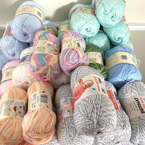 May include: A collection of yarn skeins in various colors, including pink, blue, green, and white. The yarn is arranged in a pyramid shape, with the largest skeins at the bottom and the smallest skeins at the top. The yarn is labeled "Bernat Softee Baby" and "Bee Soft Baby".