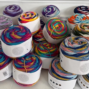 May include: A collection of colorful yarn skeins in various shades of blue, pink, yellow, and green. The yarn is neatly wound into cylindrical shapes and packaged in white paper. The image showcases a variety of yarn for knitting and crochet projects.