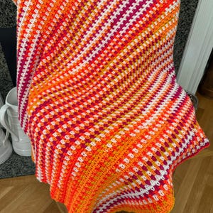 May include: A crocheted throw blanket with a diagonal pattern in shades of orange, pink, white, and yellow.