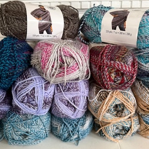 May include: A collection of colorful yarn skeins in various shades of blue, purple, gray, and brown. Some skeins have labels with a picture of a person wearing a knitted garment. The yarn is arranged in a pile, showcasing the different textures and colors.
