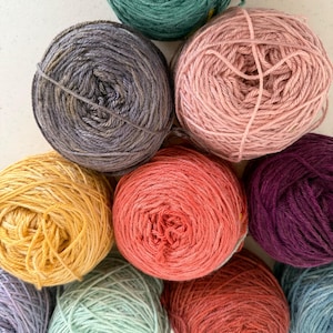 May include: A collection of ten balls of yarn in various colors, including green, purple, pink, yellow, red, and blue. The yarn is arranged in a circular pattern.