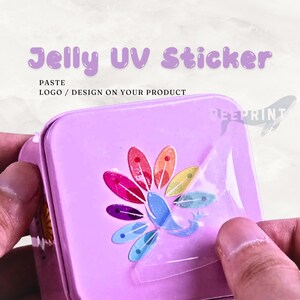 May include: A Jelly UV Sticker applied to a light purple square tin. The sticker features a colorful, fan-shaped design with a central blue whale graphic. Text on the image reads Jelly UV Sticker, PASTE LOGO / DESIGN ON YOUR PRODUCT.