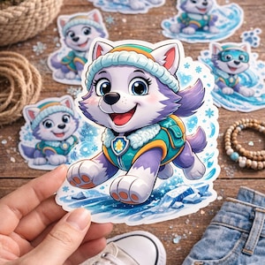 May include: A selection of cartoon stickers depicting a purple and white husky puppy wearing a teal and yellow vest and hat. The stickers are on a wooden surface with other items like sunglasses and a pair of jeans.