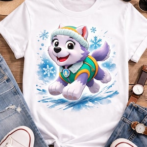 May include: White t-shirt with a cartoon husky character in a winter outfit. The husky is purple and white with a green and yellow vest and hat. Blue snowflakes and splashes of blue watercolour are in the background. The shirt is on a wooden surface.