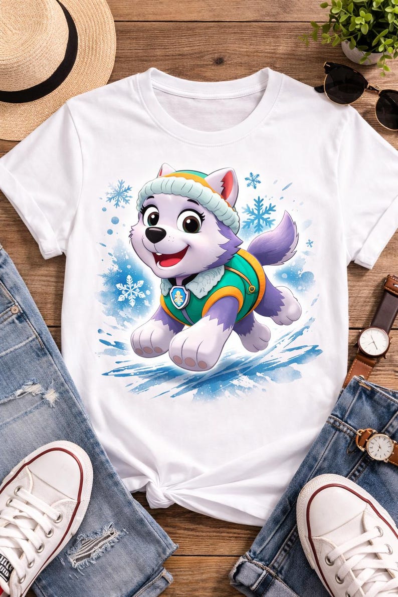 May include: White t-shirt with a cartoon husky character in a winter outfit. The husky is purple and white with a green and yellow vest and hat. Blue snowflakes and splashes of blue watercolour are in the background. The shirt is on a wooden surface.