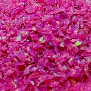 May include: Pink iridescent glitter with a holographic finish. The glitter is made of small, irregular pieces of glass.