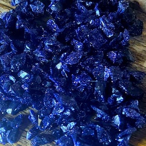 May include: A close-up of a pile of small, dark blue, sparkly, irregular shaped stones. The stones are scattered on a wooden surface.