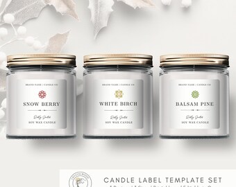 May include: Three glass jar candles with gold lids and white labels. The labels read "Snow Berry," "White Birch," and "Balsam Pine." The text "Soy Wax Candle" is below each scent name. The image also includes the text "Candle Label Template Set."