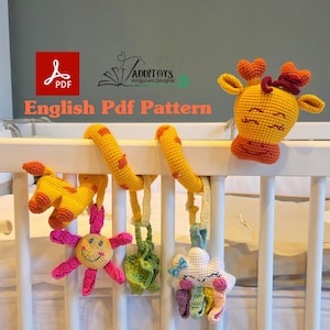 Könnte beinhalten: Handgefertigtes Baby-Mobile aus Häkelarbeit mit einer Giraffe, Sonne, Wolke und anderen Formen in Gelb, Rosa und Weiß. Das Mobile ist an einer gelben Spiralstange befestigt. Der Text "English Pdf Pattern" ist sichtbar.