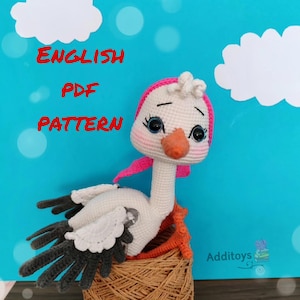 Puede incluir: Patrón de crochet para una cigüeña blanca con un lazo rosa, sentada en una cesta tejida. El patrón está disponible en formato PDF en inglés.