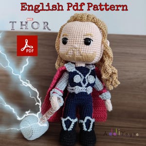 May include: Crochet pattern for a Thor amigurumi doll. The doll is wearing a red cape, blue pants, and a silver chest piece. The doll is holding a silver hammer. The pattern is available in PDF format.