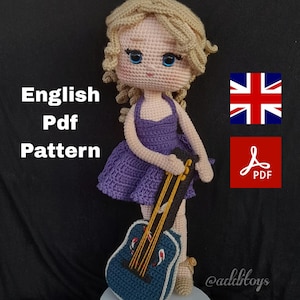 Puede incluir: Patrón de crochet para una muñeca con cabello rubio que lleva un vestido morado y sostiene una guitarra azul. El patrón está disponible en inglés y es una descarga PDF.