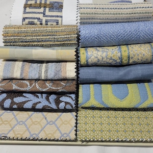 May include: A collection of fabric swatches in various patterns and colors. The swatches include geometric, floral, and textured designs in shades of blue, beige, brown, and yellow. The fabrics are arranged in a neat, organized display.