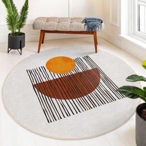 May include: A round white rug with a geometric design featuring black lines, a brown semi-circle, and a yellow circle.