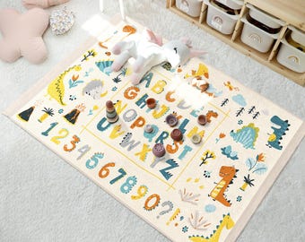 May include: A cream-colored play mat with a colorful alphabet, numbers, and dinosaur illustrations. The mat features a yellow, blue, and green color scheme.
