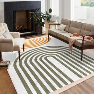 Op de afbeelding: Een wit en groen gestreept tapijt met een grote oranje en witte gestreepte cirkel in de linkerbovenhoek. Het tapijt ligt in een woonkamer met een bank en een open haard.