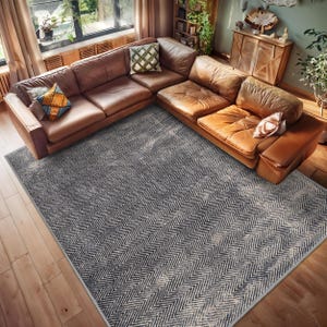 Puede incluir: Una alfombra de color gris oscuro y blanco con estampado de chevron con un sofá seccional de cuero marrón encima. El sofá tiene algunos cojines.