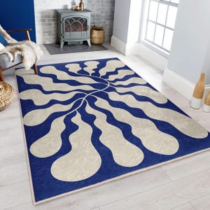 Puede incluir: Una alfombra abstracta azul y blanca con un patrón ondulado orgánico. La alfombra tiene un fondo crema con líneas onduladas azules que crean un diseño floral.