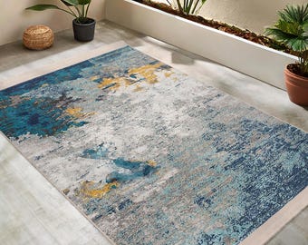May include: Abstract area rug with a blue, grey, and yellow design. The rug has a cream-coloured border.