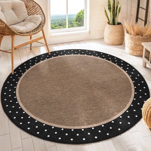 May include: A round, beige and black area rug with a white polka dot pattern around the edge. The rug has a woven texture.