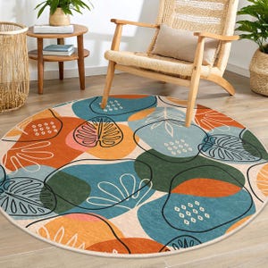 Puede incluir: Una alfombra redonda con fondo blanco y formas abstractas en tonos naranja, azul, verde y rosa. Las formas están delineadas en negro y se asemejan a hojas y otras formas orgánicas.