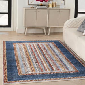 May include: A blue and beige area rug with a multi-colored striped pattern in the center. The rug has a border with a geometric design.
