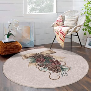 May include: A round beige rug with a brown and green pine cone and bow design. The rug is on a wooden floor in a room with a white wicker chair.