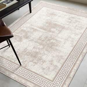 May include: A beige area rug with a white Greek key border. The rug has a distressed, vintage look.