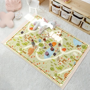 Puede incluir: Una alfombra de juego verde y marrón con un camino sinuoso y varios animales del bosque, incluyendo ciervos, osos y ardillas. La alfombra tiene un borde rosa y está decorada con pequeñas flores y hojas.