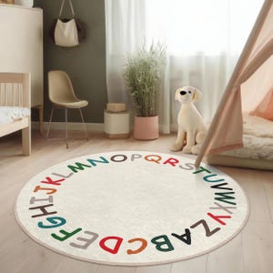 May include: A white round rug with a colorful alphabet border. The rug is on a light wood floor in a room with a white tent, a chair, and a potted plant.