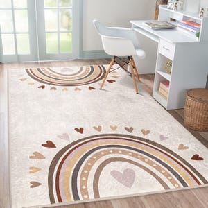 May include: A beige area rug with two brown and beige rainbows and brown hearts. The rug has a light brown background with a subtle texture.