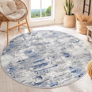 Può includere: Un tappeto rotondo astratto blu e grigio con un aspetto usurato e sbiadito. Il tappeto ha un bordo bianco.