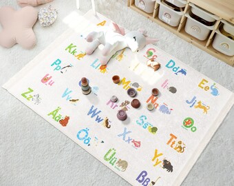 May include: A white play mat with colorful letters of the alphabet and animal illustrations. The letters are in a variety of colors and the animals are drawn in a cartoon style. The mat is on a white surface and there are some toys on the mat.