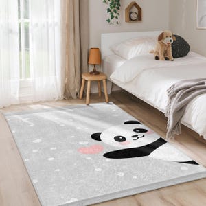 Könnte beinhalten: Ein grauer und weißer Pandabären-Teppich mit einem rosafarbenen Herzdesign. Der Teppich hat einen Fransenrand und liegt auf einem grauen Boden.