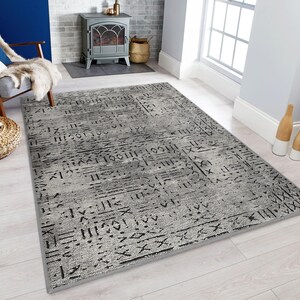 May include: A grey and black area rug with a geometric pattern. The rug has a distressed look and features a variety of lines and shapes.
