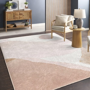 Könnte beinhalten: Ein hellrosa und weißer Teppich mit geometrischem Muster, das abstrakte Formen und eine dezente Textur aufweist. Der Teppich liegt auf einem Holzboden in einem Wohnzimmer.