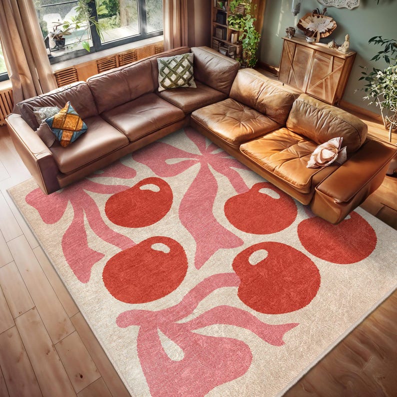 May include: A cream-coloured rug with a pink and red cherry design. The rug features stylised pink leaves and red cherries with a textured surface.