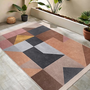 May include: A geometric patterned rug with a mix of pink, brown, gray, and gold colors. The rug has a modern design with a variety of shapes and sizes.