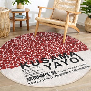 May include: A round, white rug with a red polka dot pattern. The rug has the text "KUSAMA YAYOI" in black letters. The text below the name reads "草間彌生展 ワタシというナニモノかへの問い 2010.9.18 11.7 武蔵野市立吉祥寺美術館".