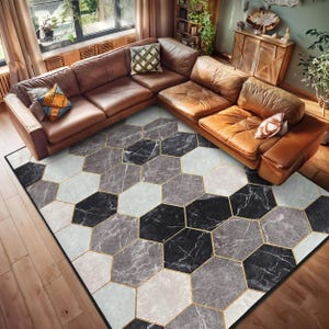May include: A brown leather sectional sofa with a geometric patterned rug in shades of gray and black with gold accents. The rug has a hexagonal pattern.