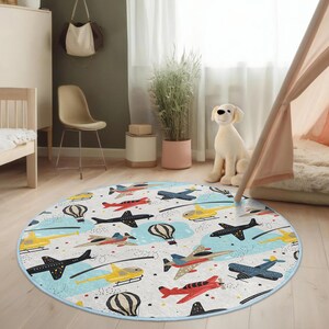 May include: A round, blue-edged play rug with a white background and a colorful pattern of airplanes, hot air balloons, and stars. The rug is perfect for a child's playroom or bedroom.