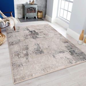Puede incluir: Una alfombra beige con un patrón abstracto desgastado en tonos grises y negros. La alfombra tiene un borde de flecos sutil.