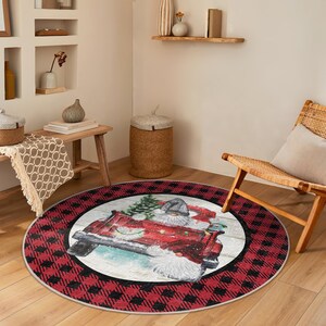 Puede incluir: Una alfombra redonda con un borde de cuadros rojos y negros. El centro presenta una ilustración de acuarela de Papá Noel en un camión rojo que transporta un árbol de Navidad. La alfombra es adecuada para una sala de estar o un dormitorio.