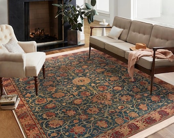 May include: A blue, red, and beige patterned rug with a floral design. The rug is laid out on a hardwood floor in a living room setting with a couch and a fireplace.