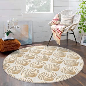 May include: A round cream-coloured rug with a repeating pattern of beige seashells. The rug is in a room with a white wicker chair and a potted plant.