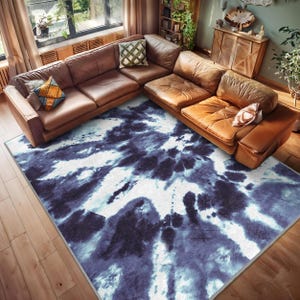 May include: A blue and white tie-dye area rug with a modern abstract design. The rug is placed in a living room with a brown leather sectional sofa.