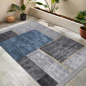 May include: A modern geometric area rug with a blue, grey, and gold colour scheme. The rug has a textured surface and a contemporary design.