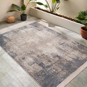 May include: A contemporary abstract area rug with a distressed, faded look. The rug features a blend of beige, gray, and blue tones, creating a subtle and sophisticated design.